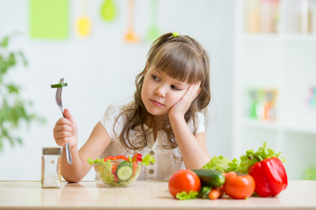A young girl staring at her salad meal that she doesn't want to eat in the kitchen